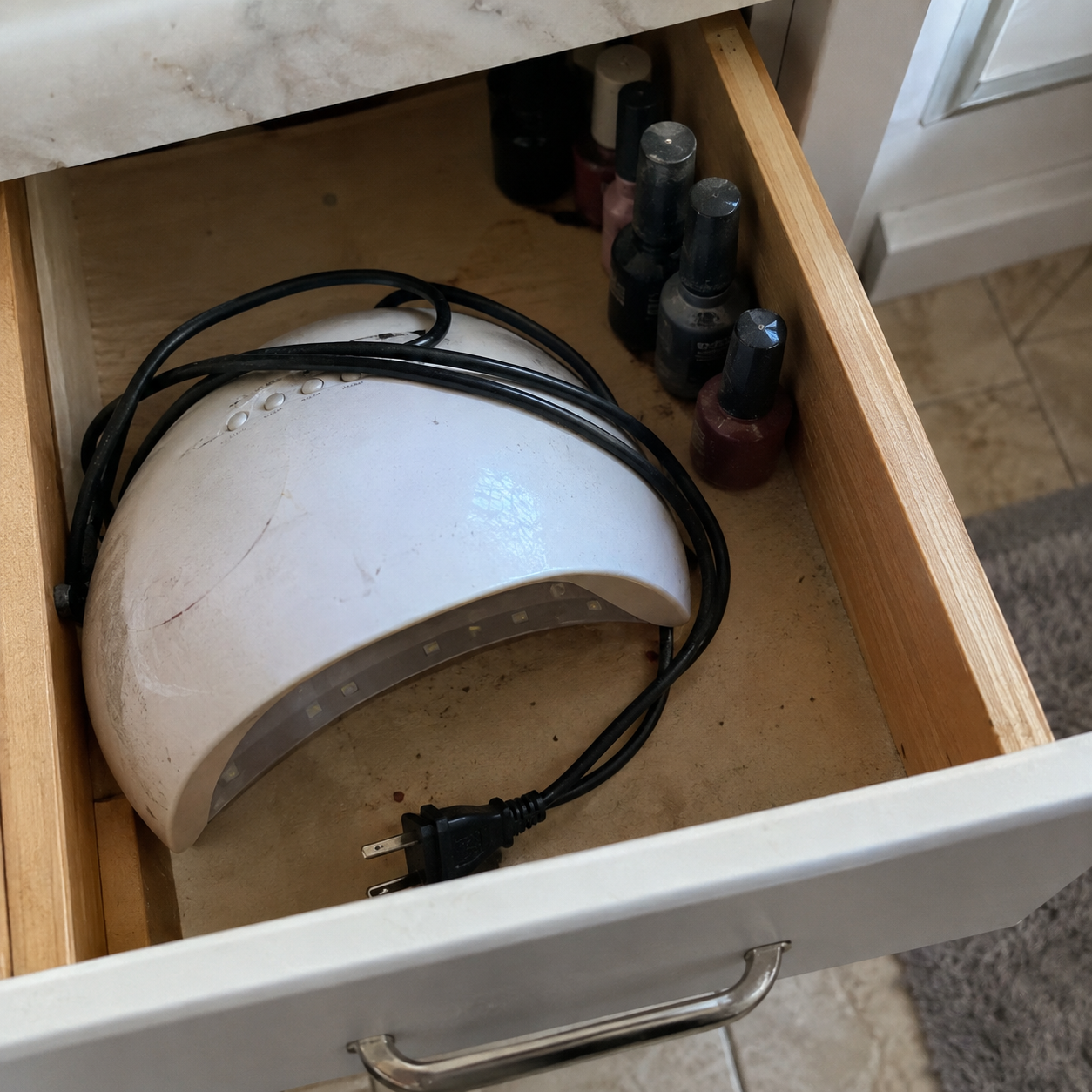 An unplugged UV nail lamp pushed to the back of a drawer